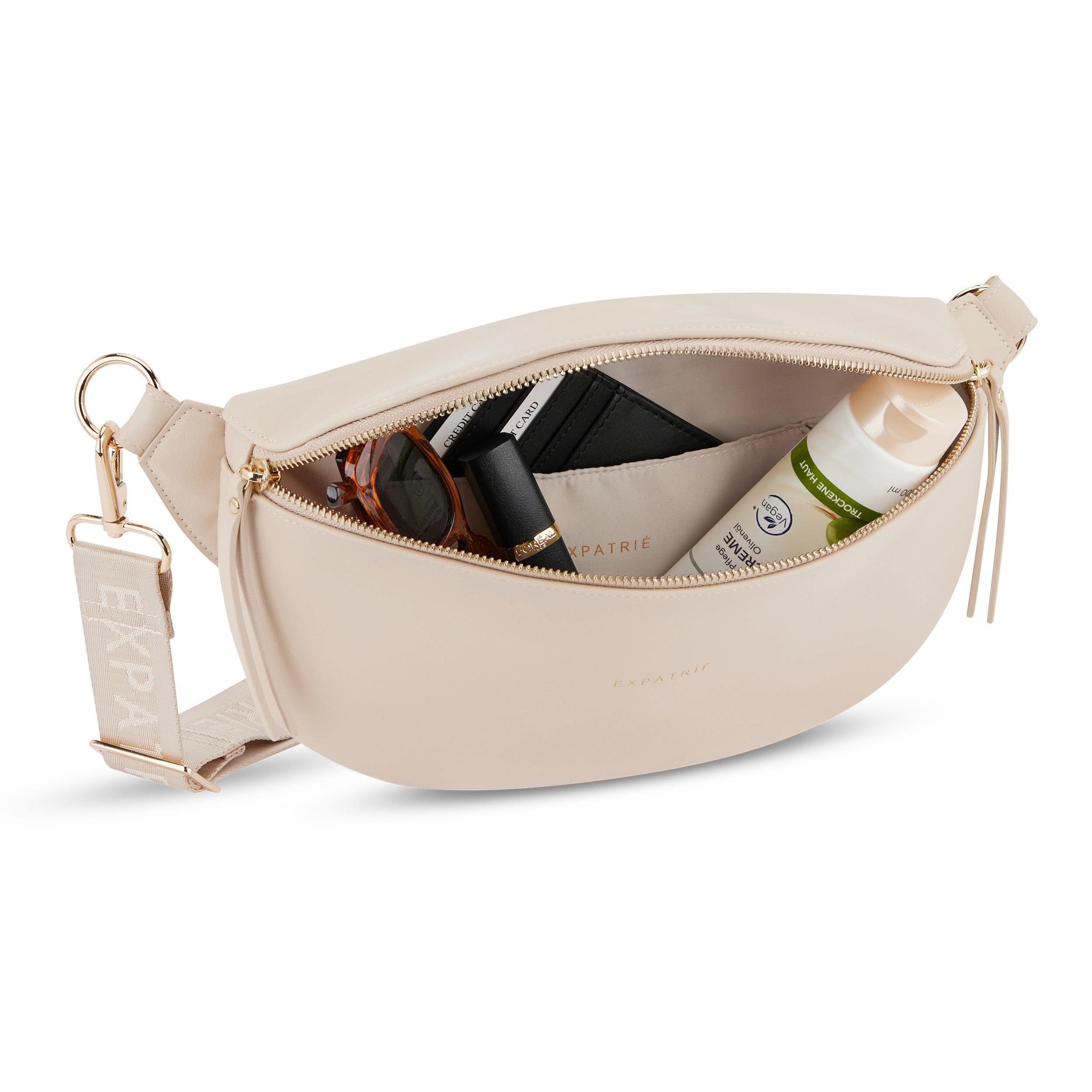 Beige Bauchtasche Alice Medium aus Leder mit geöffnetem Reißverschluss und sichtbaren Innenfächern, mit Sonnenbrille, Lippenstift, Kartenetui und Creme gefüllt