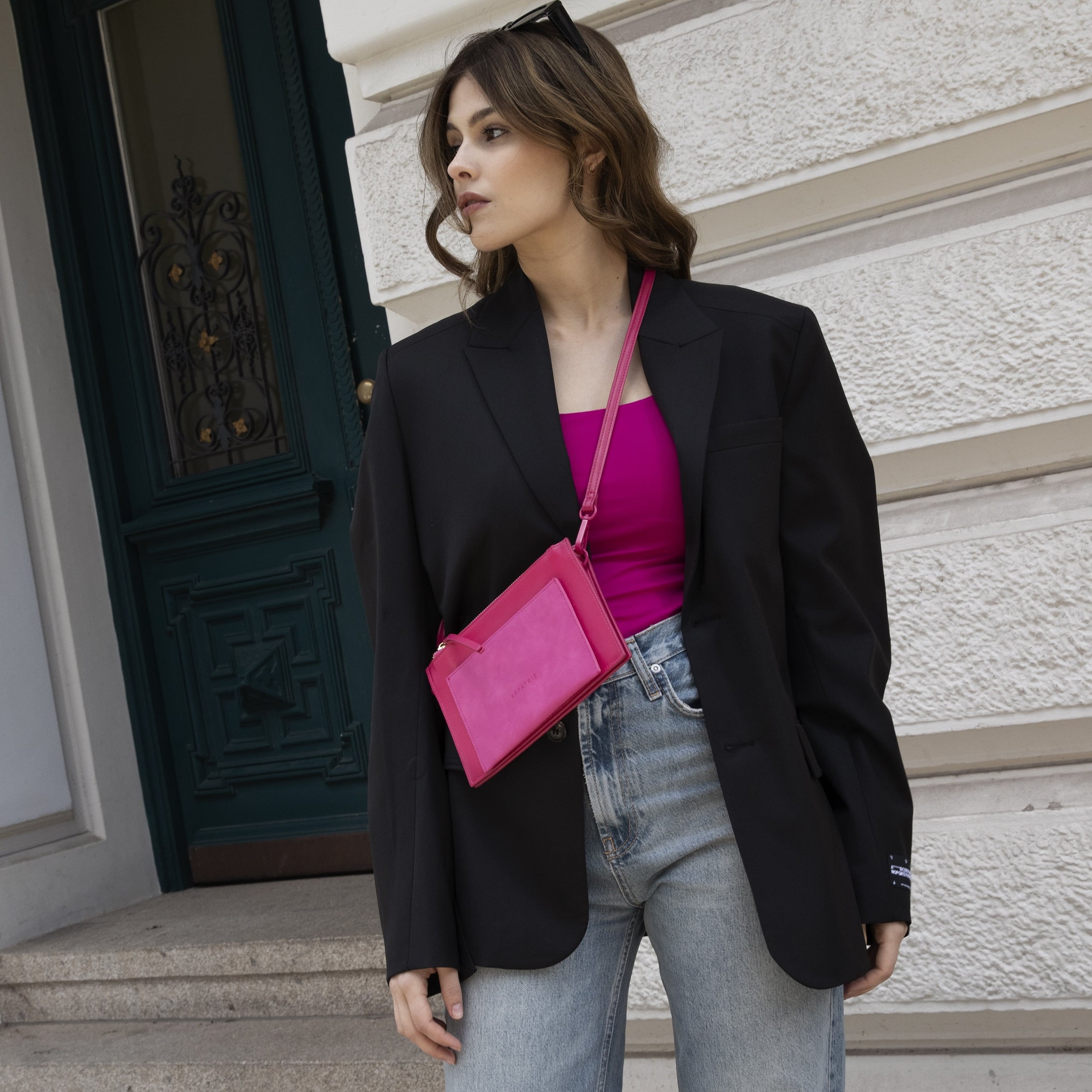 Frau mit schwarzem Blazer, pinkem Top und hellblauer Jeans trägt rosa Clutch Isabelle als Umhängetasche
