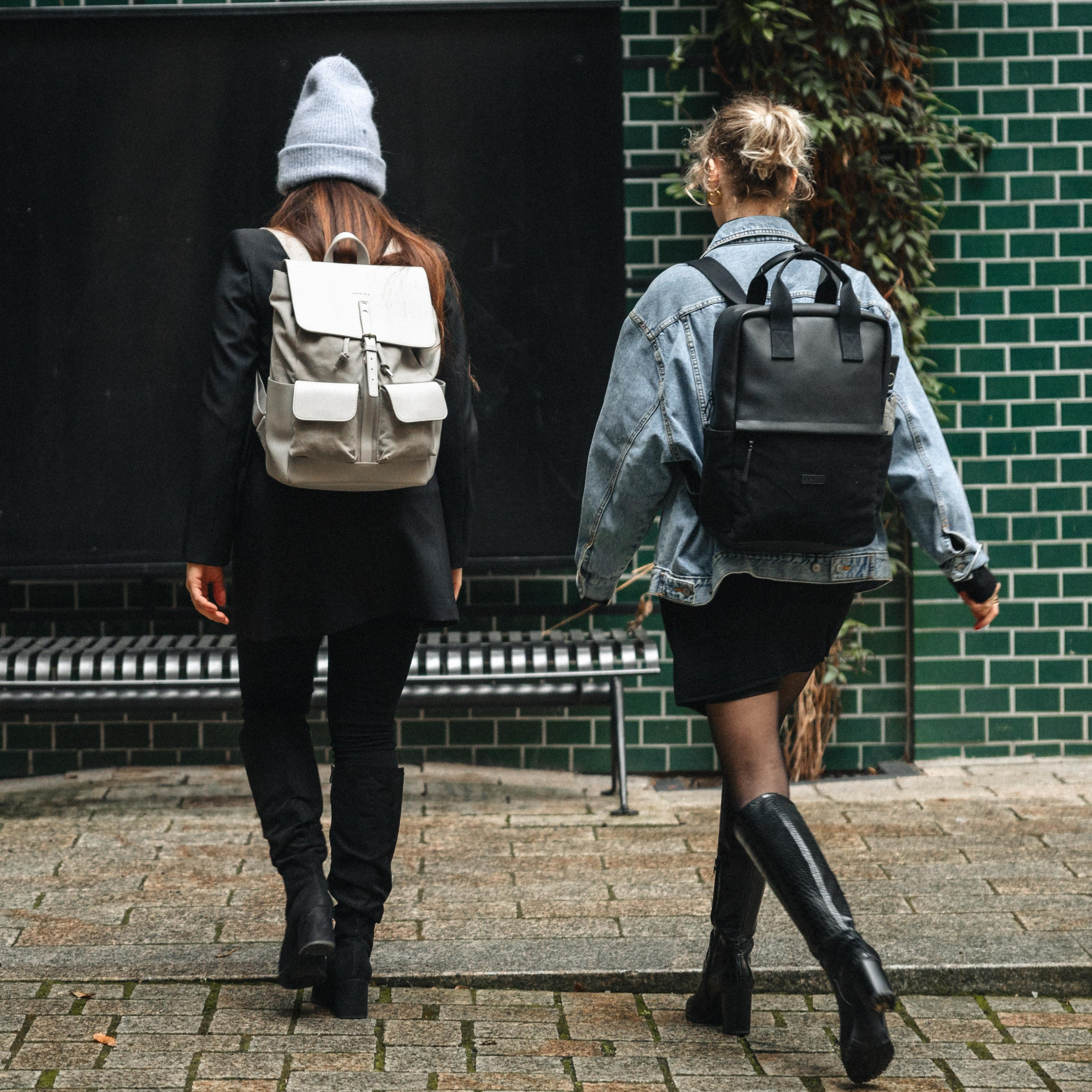 Zwei Frauen von hinten gehen, eine trägt einen hellen Canvas-Leder Rucksack Mila, die andere einen schwarzen Rucksack, urbanes Umfeld