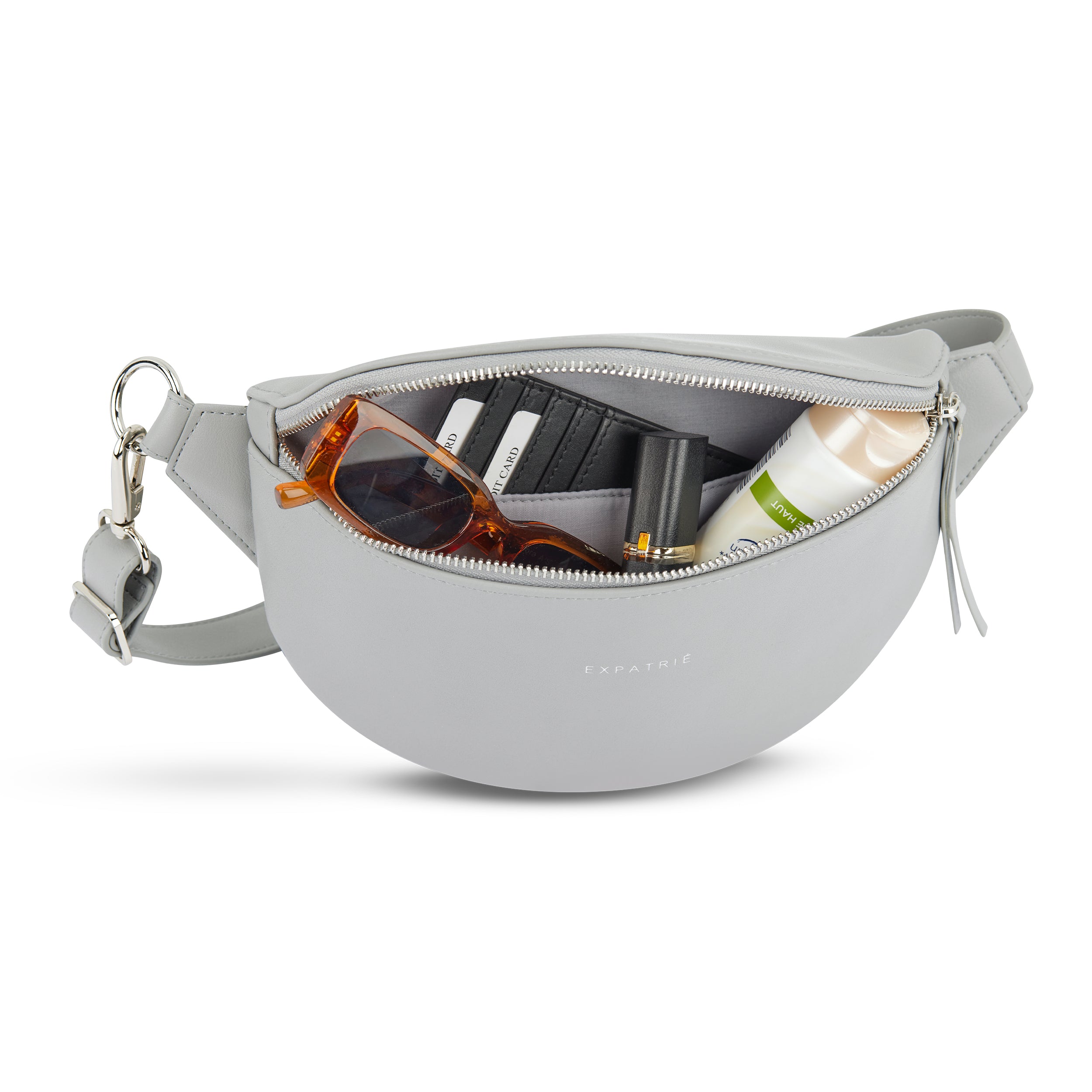 Graue Bauchtasche Alice Small mit geöffnetem Reißverschluss, zeigt Sonnenbrille, Geldbörse, Lippenstift und Creme