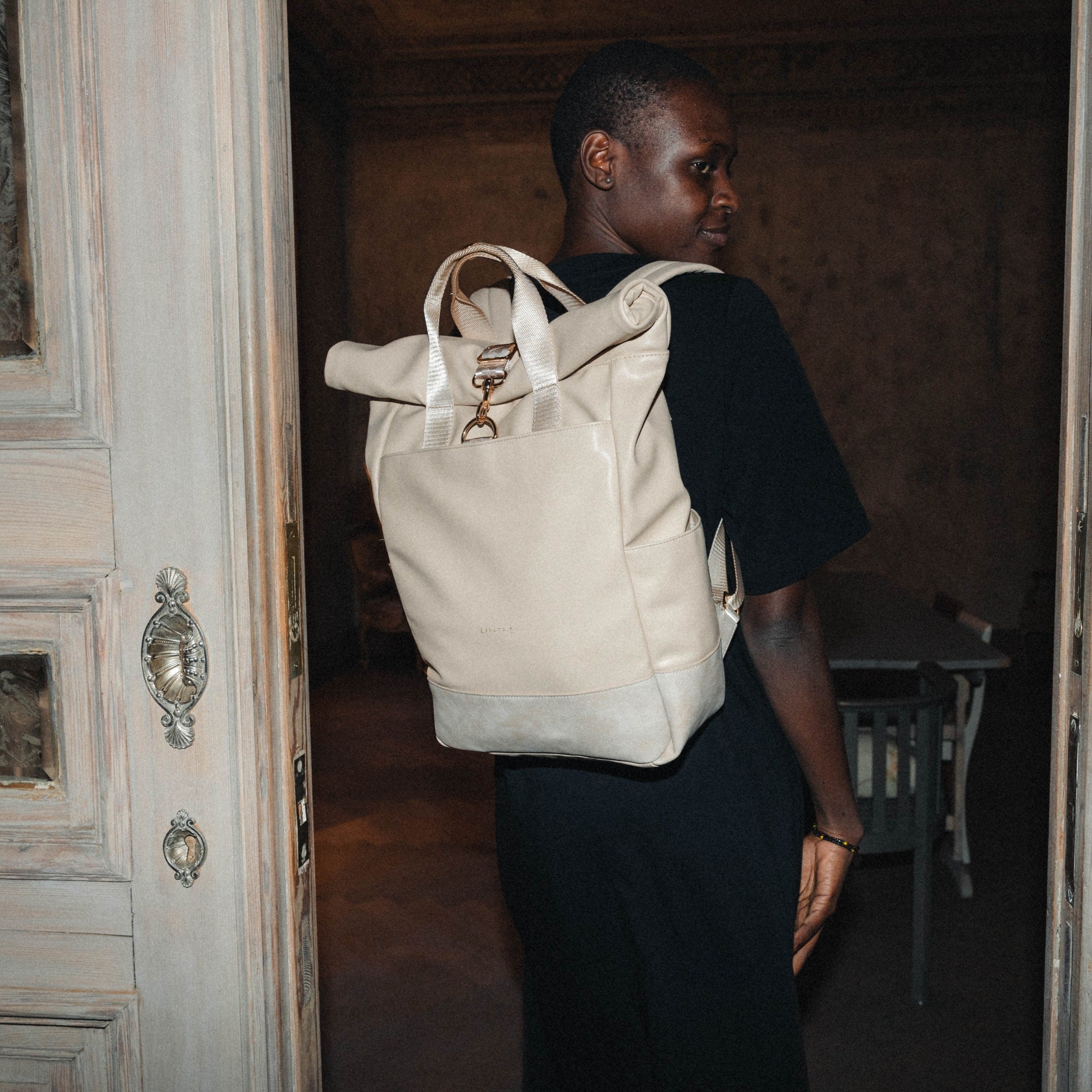 Frau trägt beige Rolltop Rucksack Adele aus Leder mit Metallverschluss