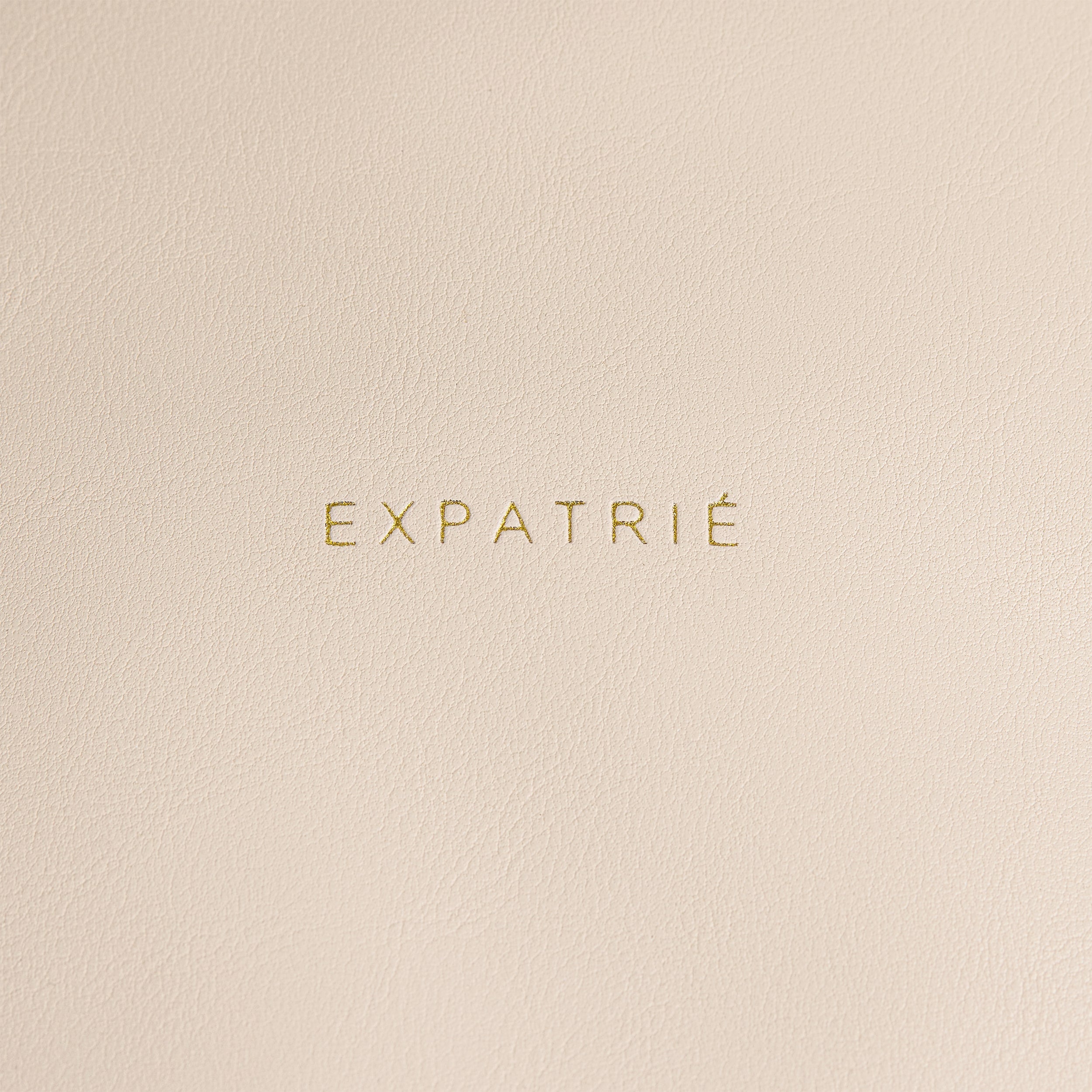 Goldene Prägung 'EXPATRIÉ' auf beigem Kunstleder des Rolltop Rucksacks Adele